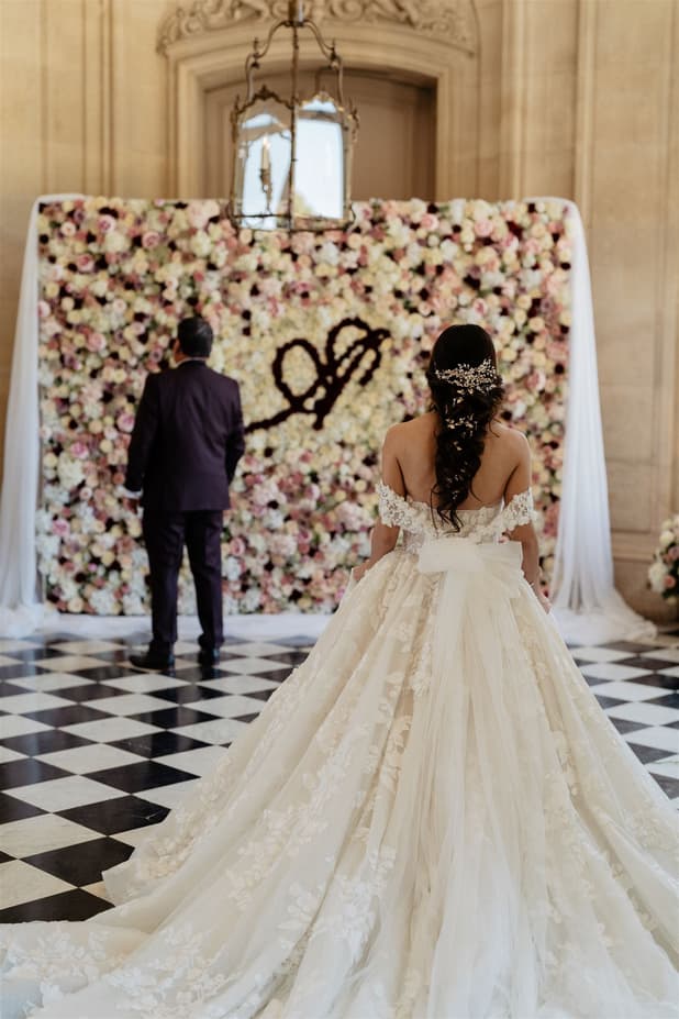 A wall of blush, cream and burgundy roses with the couple’s initials in dark roses, on checkerboard marble