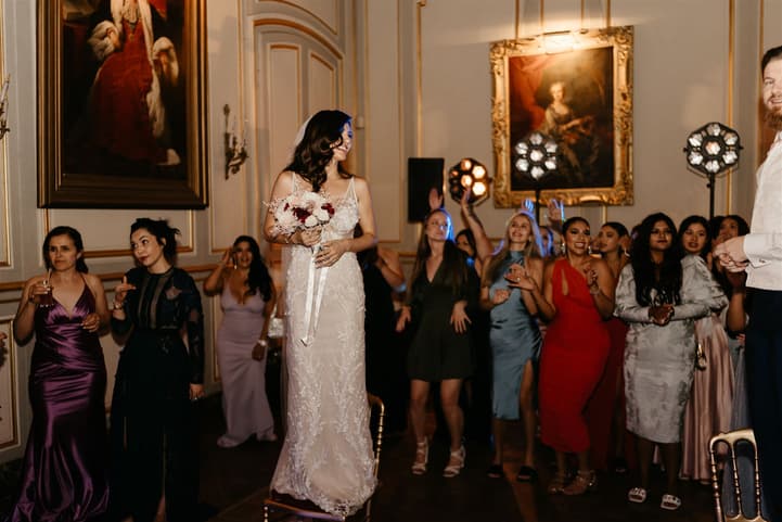 The bride about to throw her bouquet of cream and burgundy roses, the guests waiting behind her