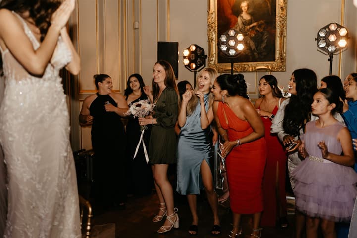 Wedding guests reaching for the bridal bouquet of cream and burgundy roses on the dance floor