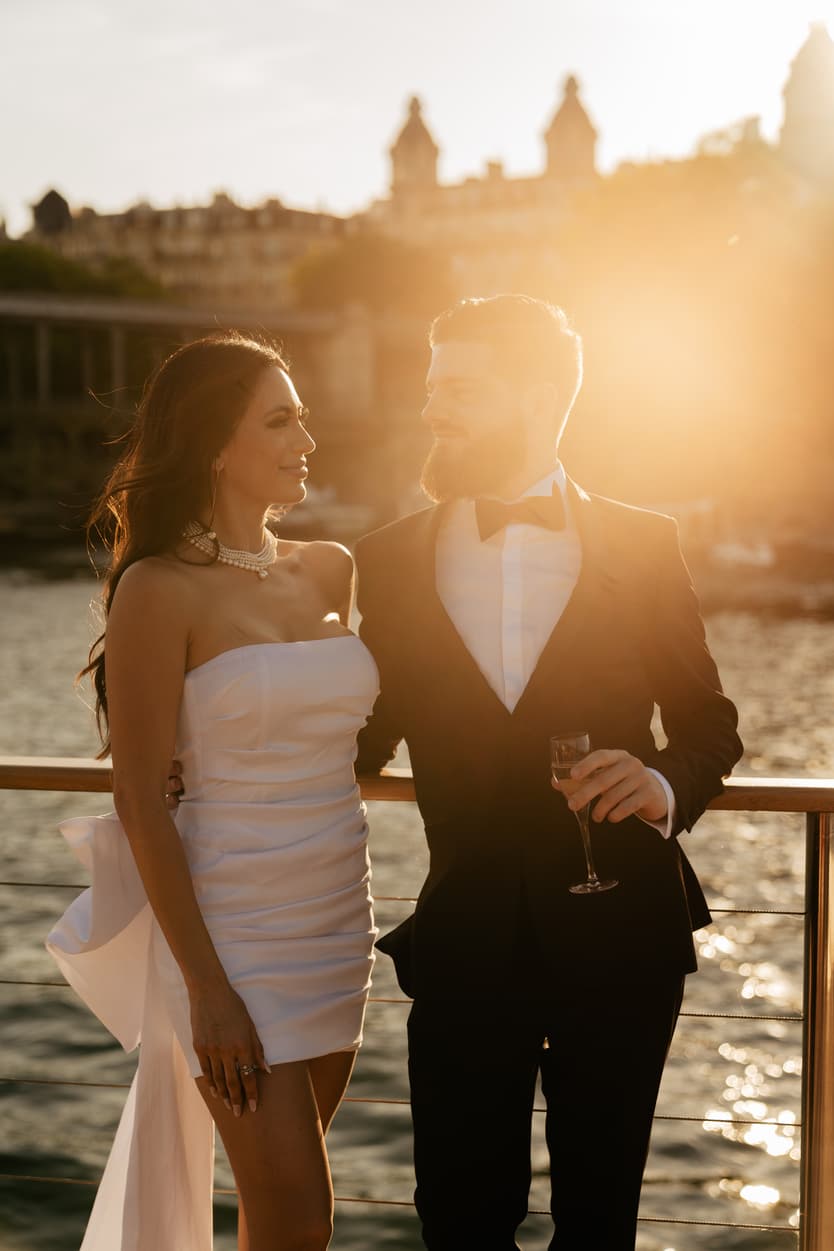 Bride and groom on deck in the low sun, a glass of champagne in his hand at the welcome dinner