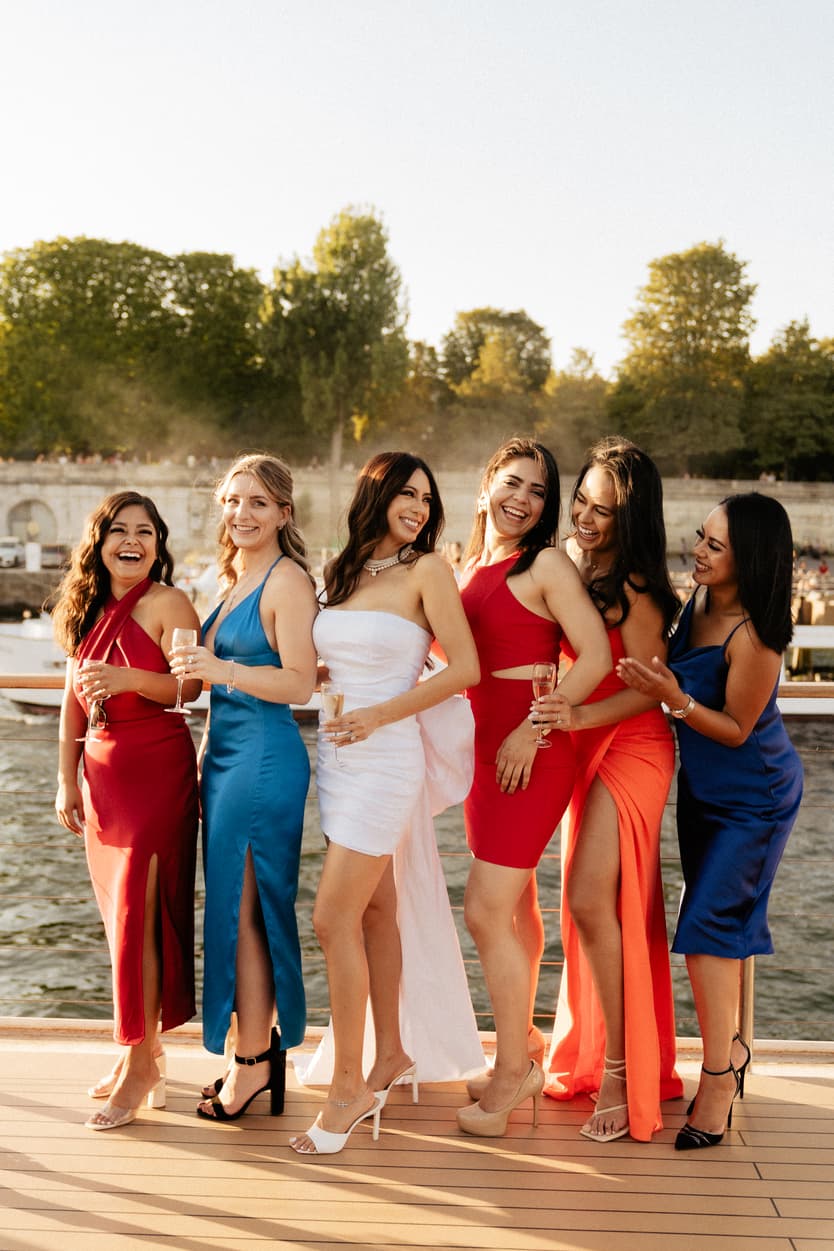 Bridesmaids in red, blue and orange lined up with the bride at the welcome dinner on the Seine