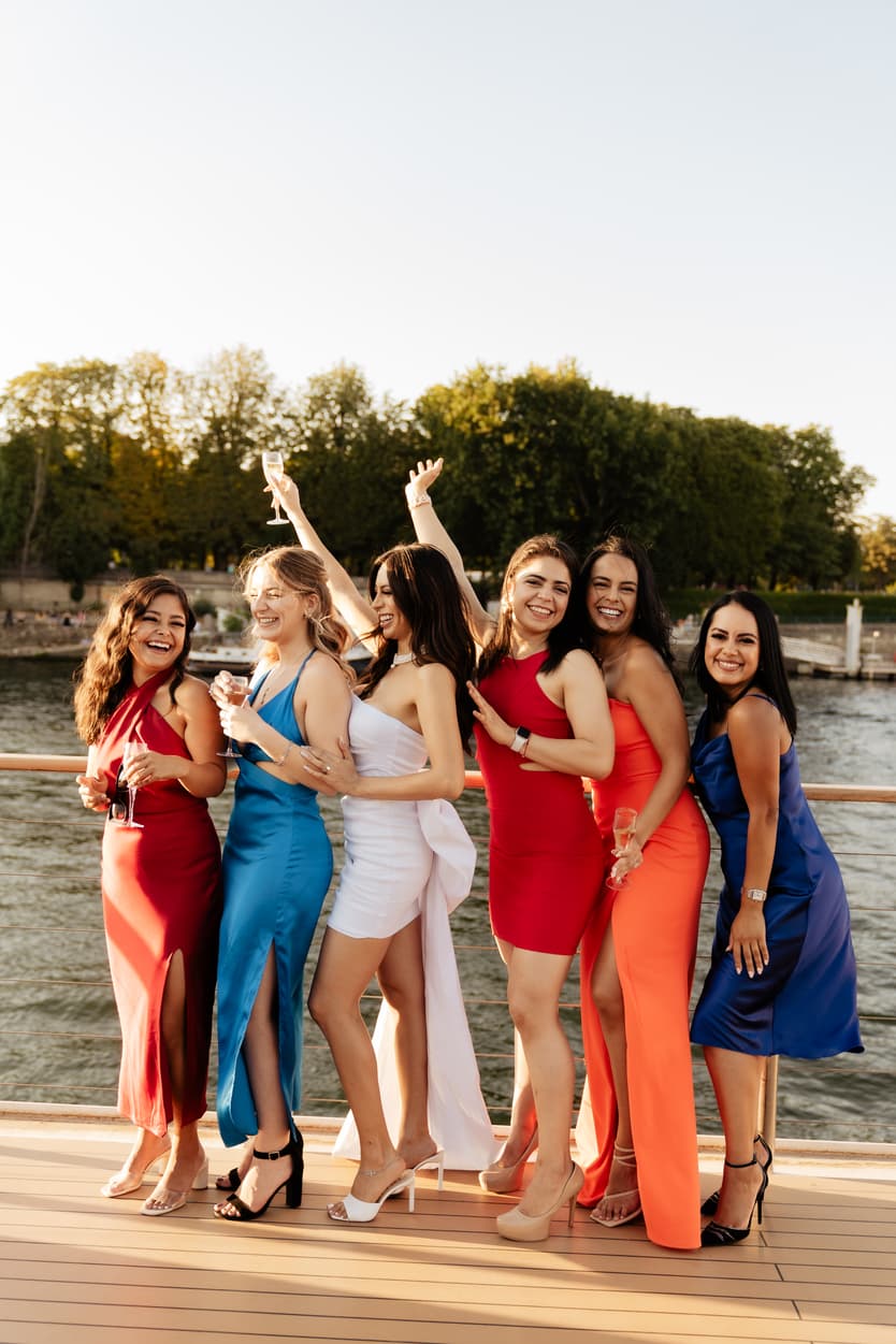The bride with her bridesmaids in red, blue and orange dresses on the deck of the boat