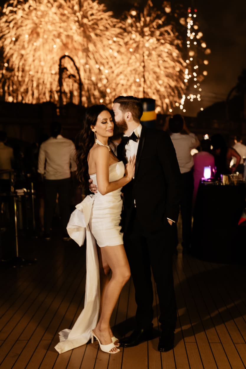 The couple under the 14 July fireworks on the deck, her white dress lit by them