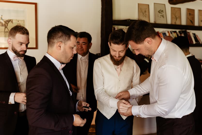 The groom having his waistcoat buttoned by his groomsmen before the wedding