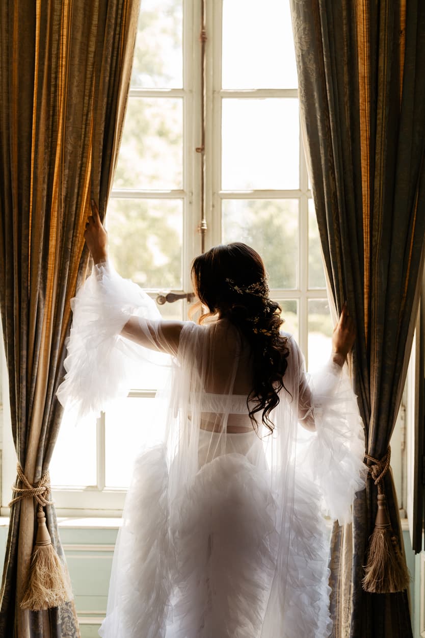 The bride at the window in a ruffled tulle robe before the wedding dress goes on