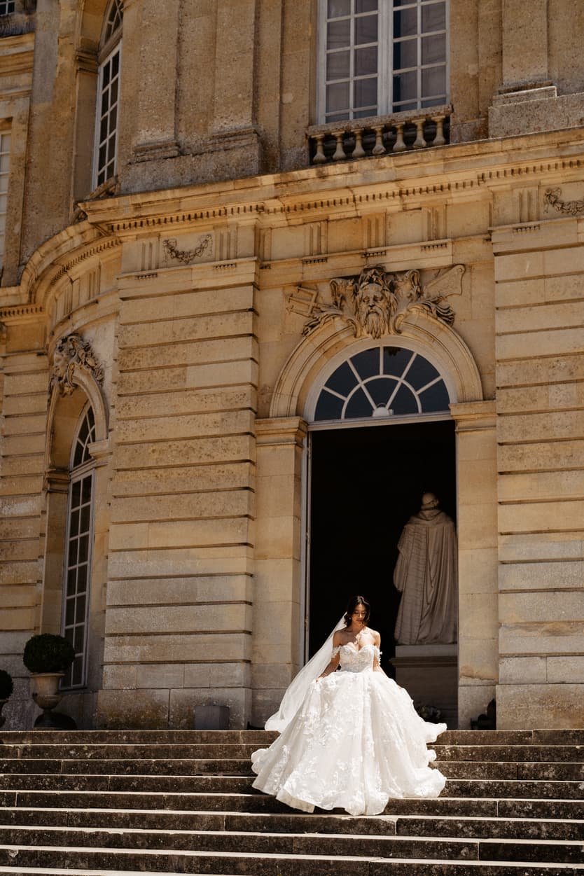 The bride coming down the château steps in her lace ball gown, the cathedral train behind her