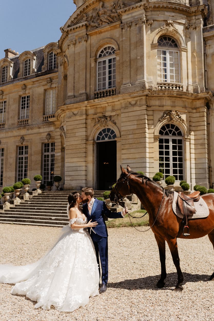 The couple kissing beside the horse, her lace ball gown spread over the gravel