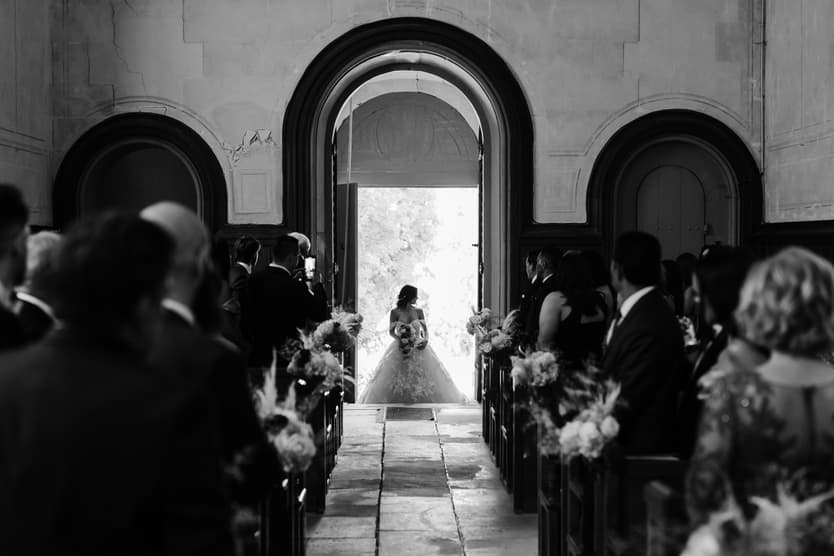 The church aisle in black and white, the bride and her wedding dress in the doorway at the far end