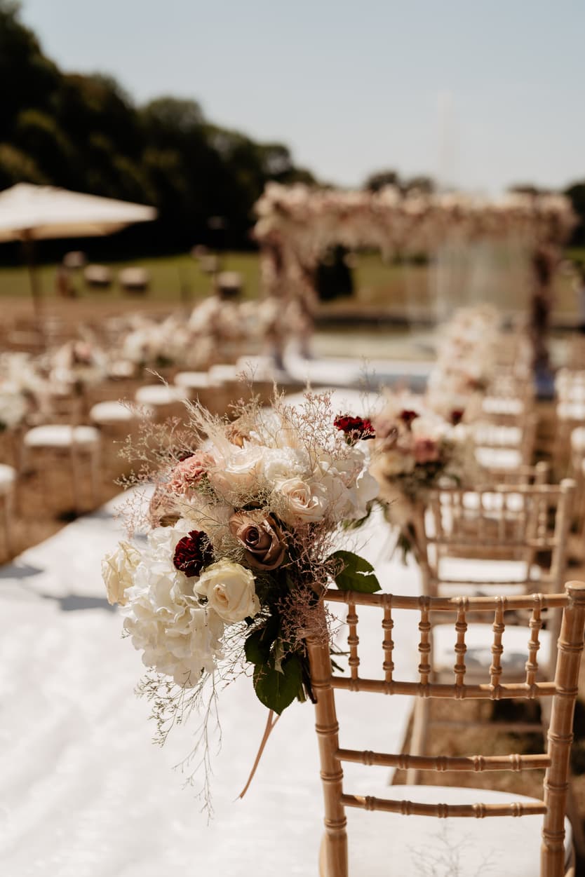The bridal bouquet of blush and burgundy roses left on a gold chiavari chair by the aisle