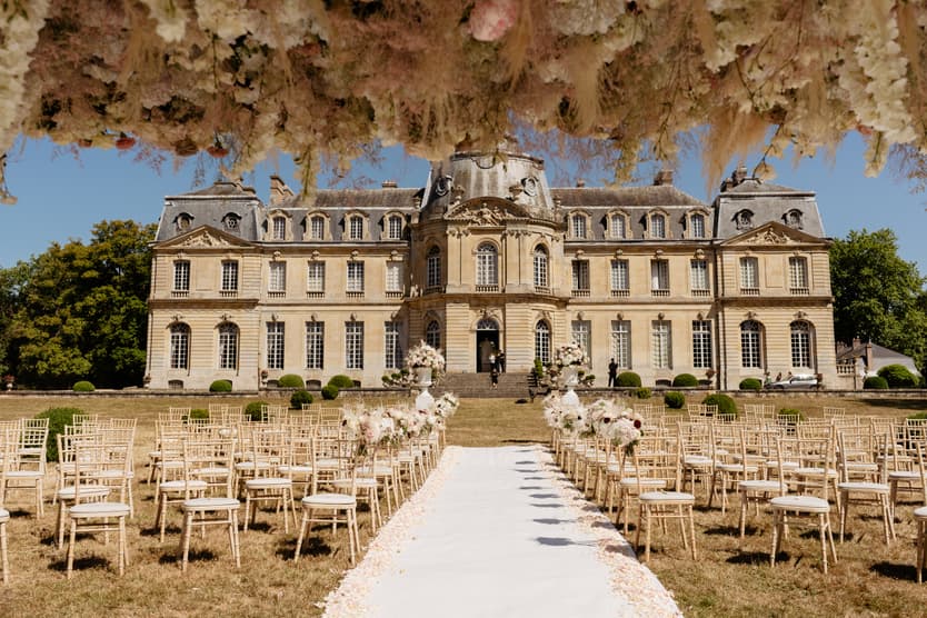 Hanging flower canopy of pampas grass, dried stems and blush roses over the aisle, gold chairs on the château lawn