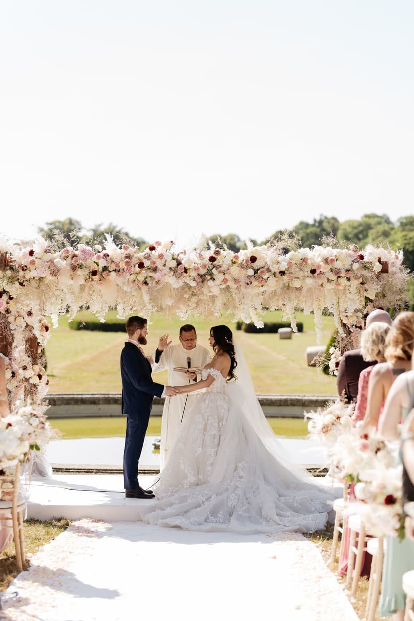 Bride and groom holding hands under the flower arch during the outdoor ceremony