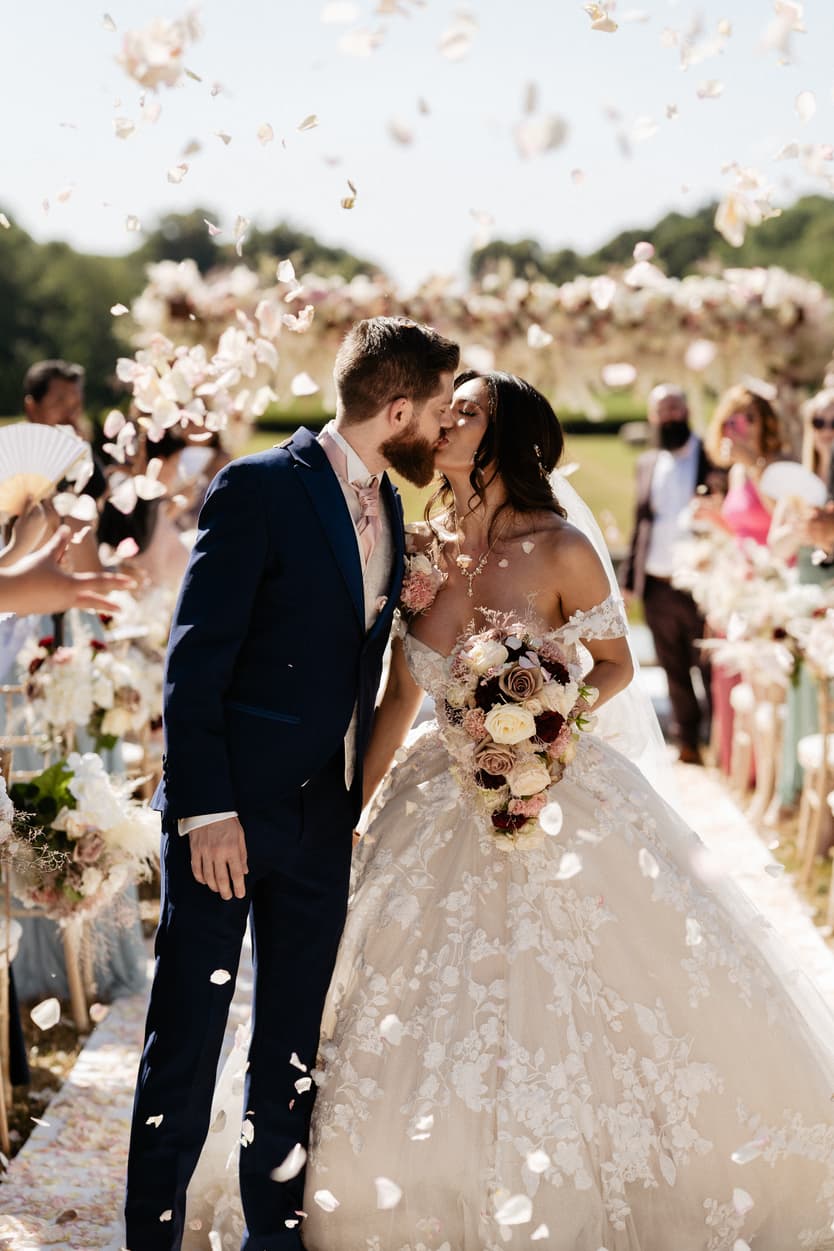 Bride and groom kissing in the aisle while their guests throw petals over them