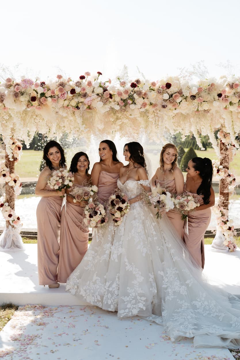 The bride with her bridesmaids in dusty-rose satin, all holding bouquets of blush roses