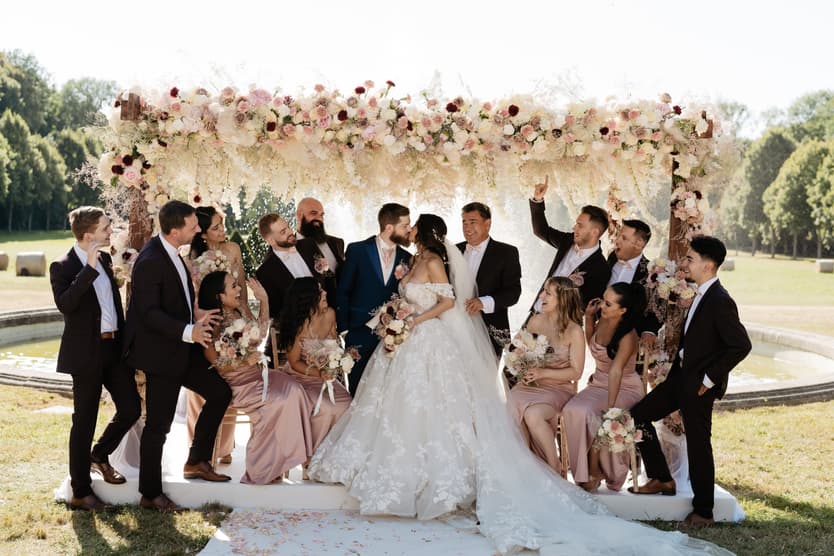 The whole wedding party on the lawn under the arch, hands in the air