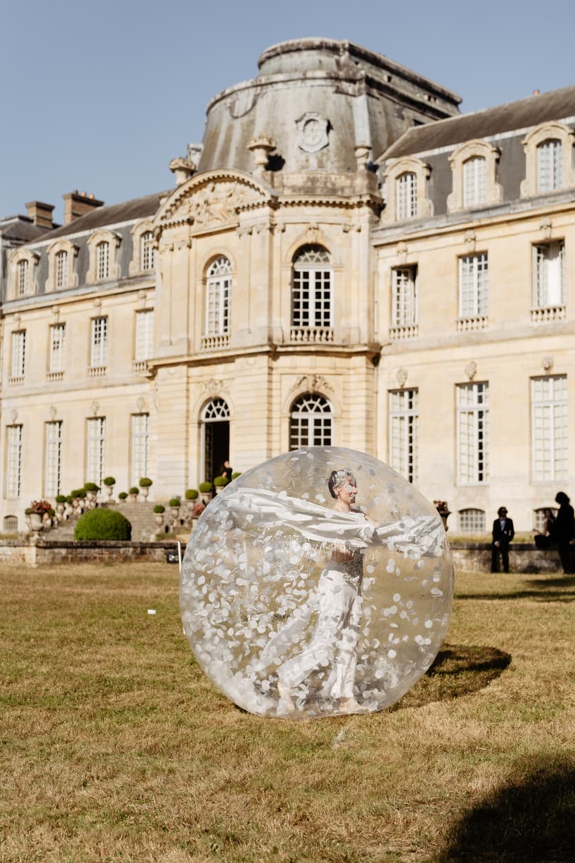 A guest rolling across the lawn inside a giant transparent ball, the château behind