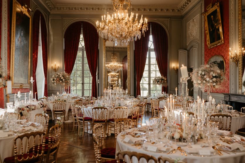 The reception in the red salon: round tables, gold chairs and tapered candles under the chandeliers