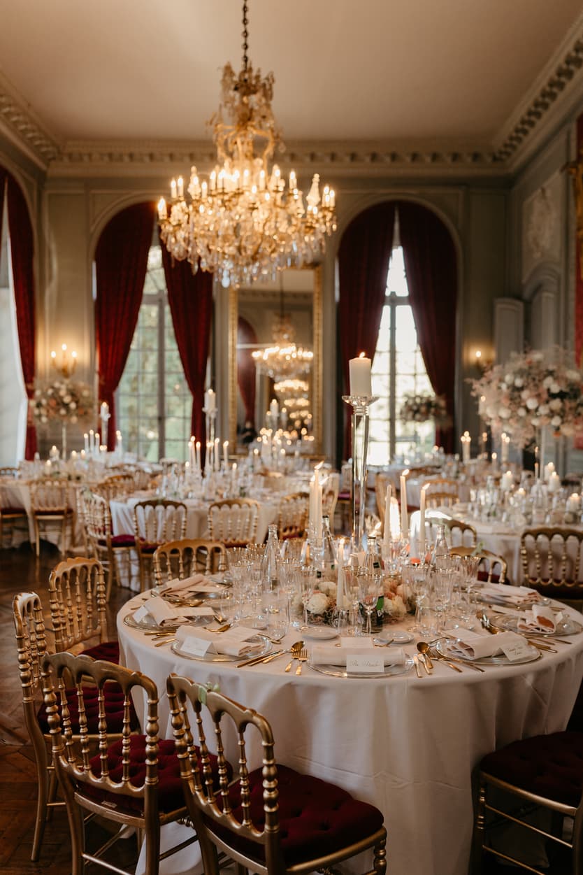 The wedding tables laid under the crystal chandelier, blush roses and candlelight on white linen