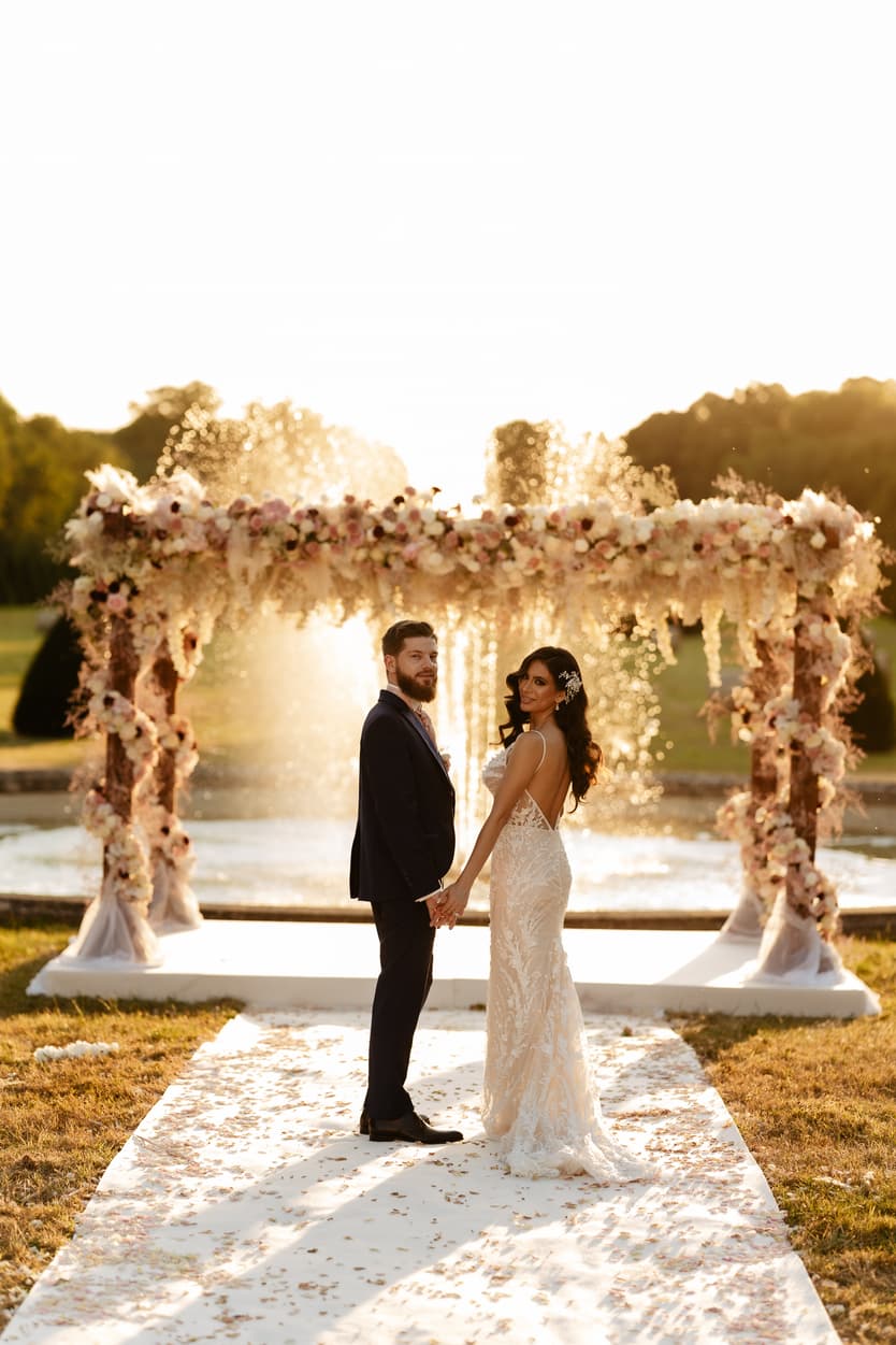 Bride and groom kissing in the park at sunset, her fitted lace evening gown in the golden light