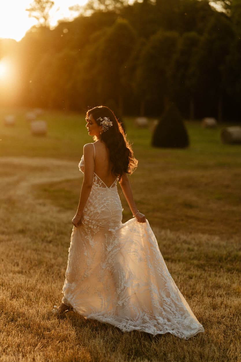 The bride walking away through the park at sunset, her lace evening gown trailing in the golden light