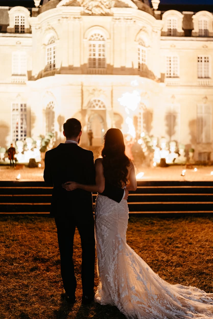 The couple watching the fire show from the lawn, the château lit behind them