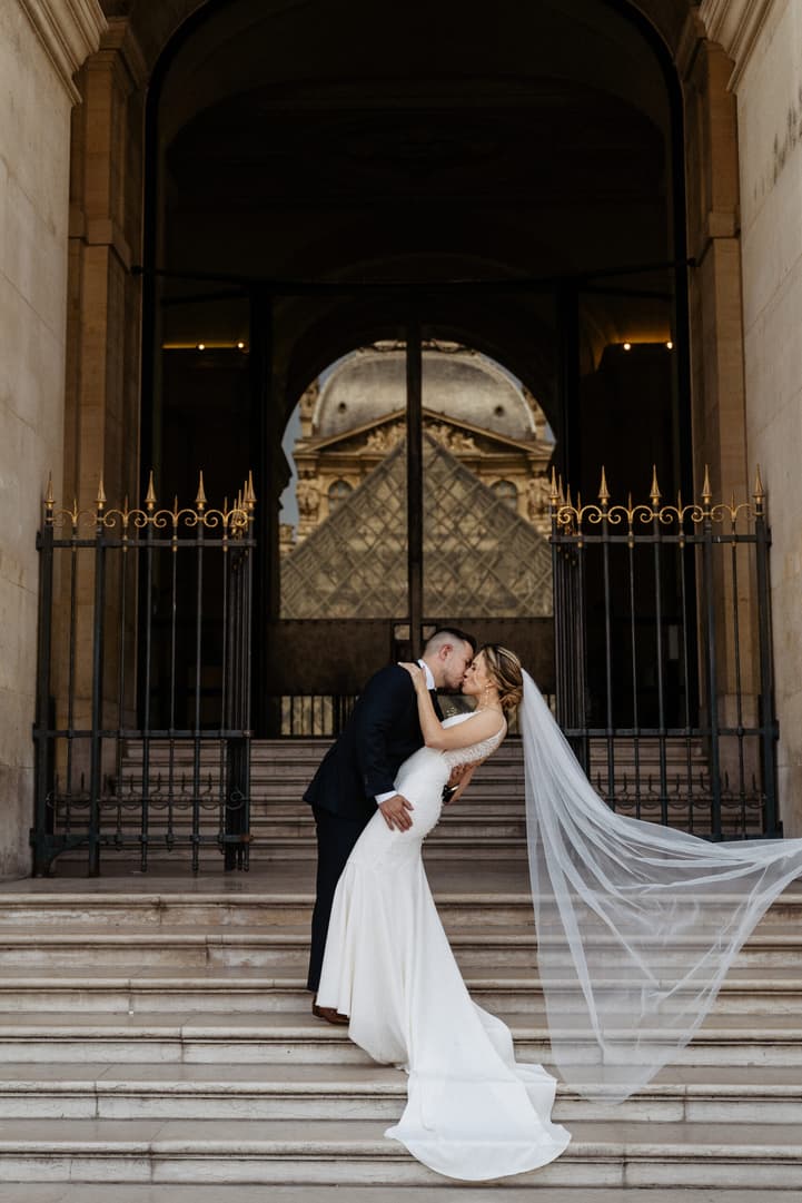 groom and bride kissing next to pyramide at Louvre