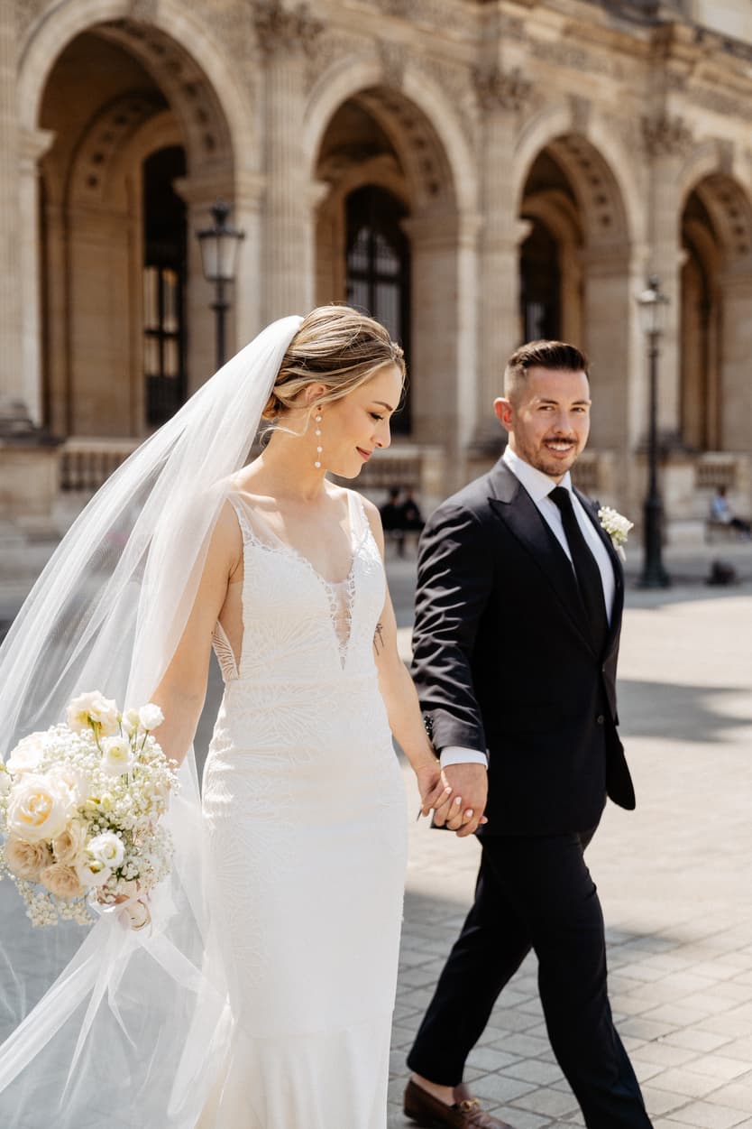 groom and bride walking hand in hand at Louvre