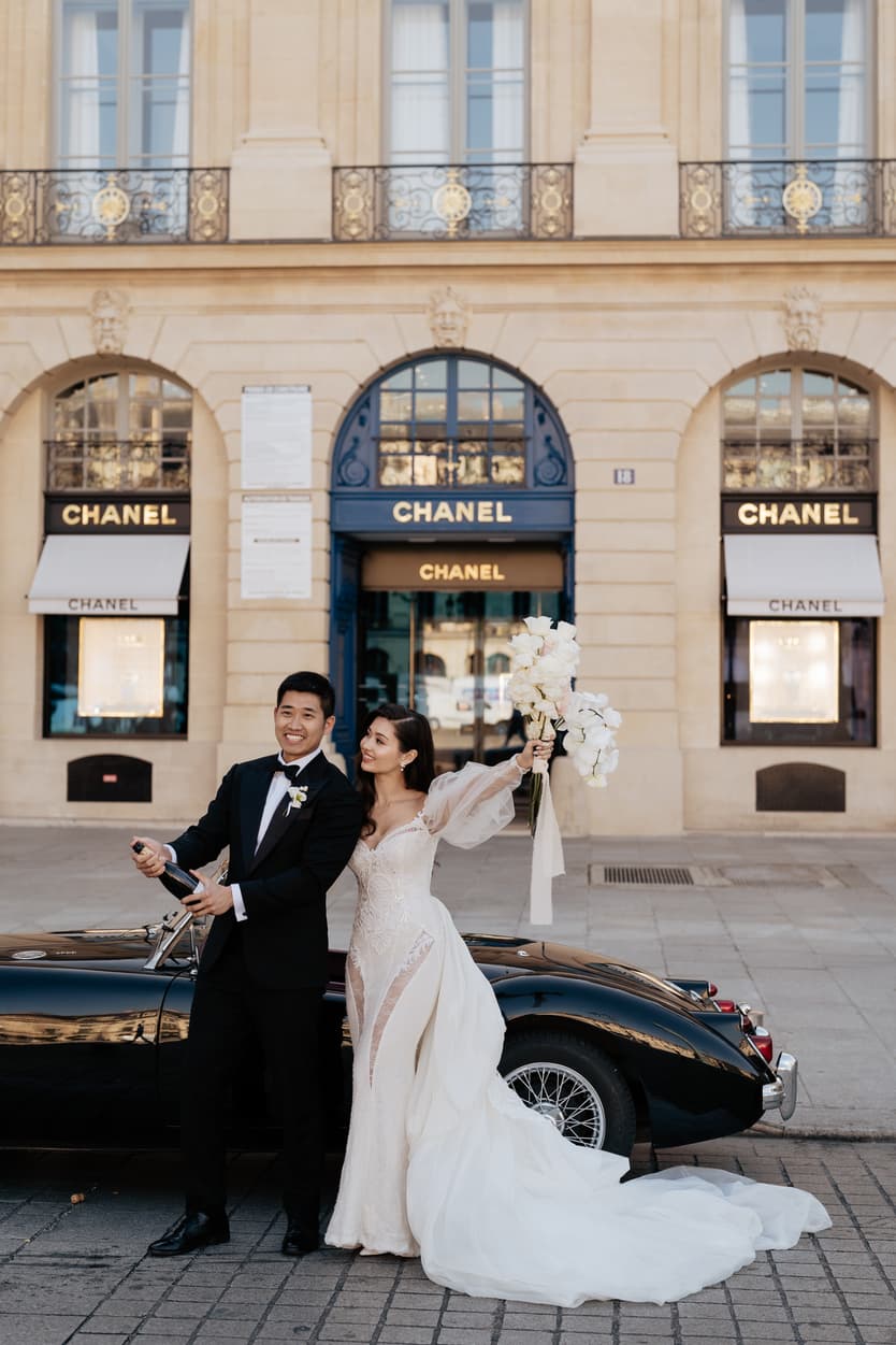 A bride and groom beside a dark vintage car in front of Chanel on the place Vendôme