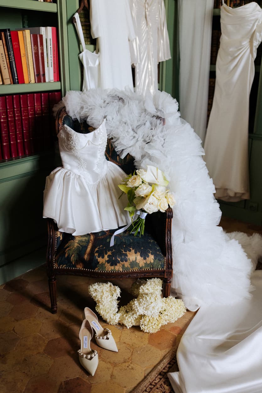 Wedding dress and the bride’s ruffled robe hanging in the library at Château du Grand Lucé, shoes and bouquet below