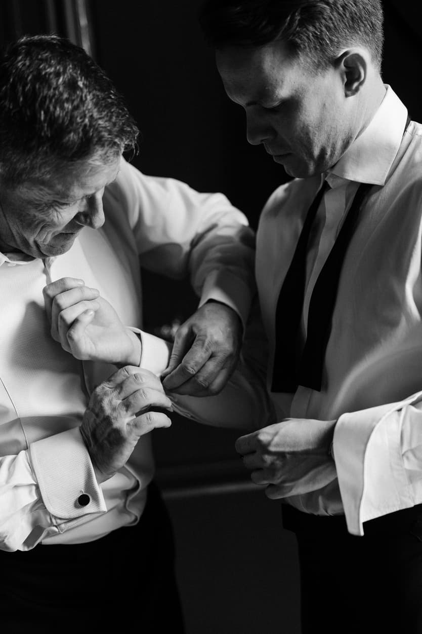 A groomsman fastening the groom’s cufflink in black and white before the château wedding ceremony