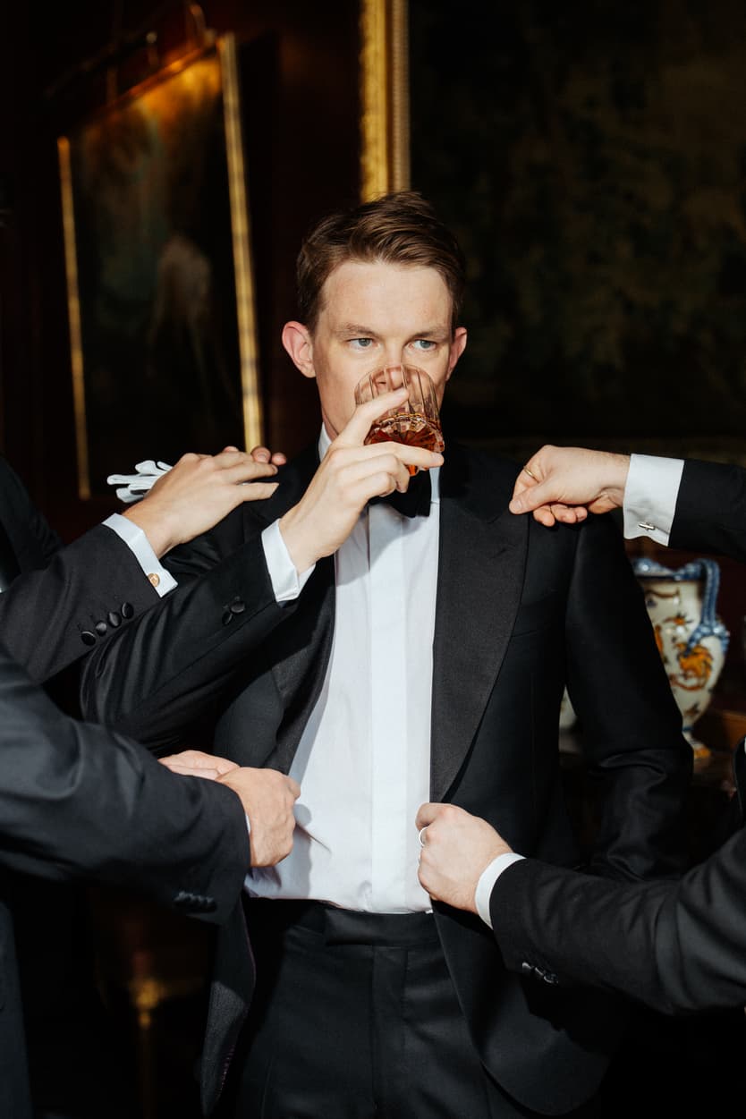 The groom straightening his black bow tie in the red room at Château du Grand Lucé