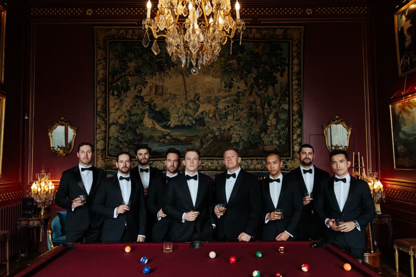 Groomsmen in black tie along the billiard table in the red room at Château du Grand Lucé