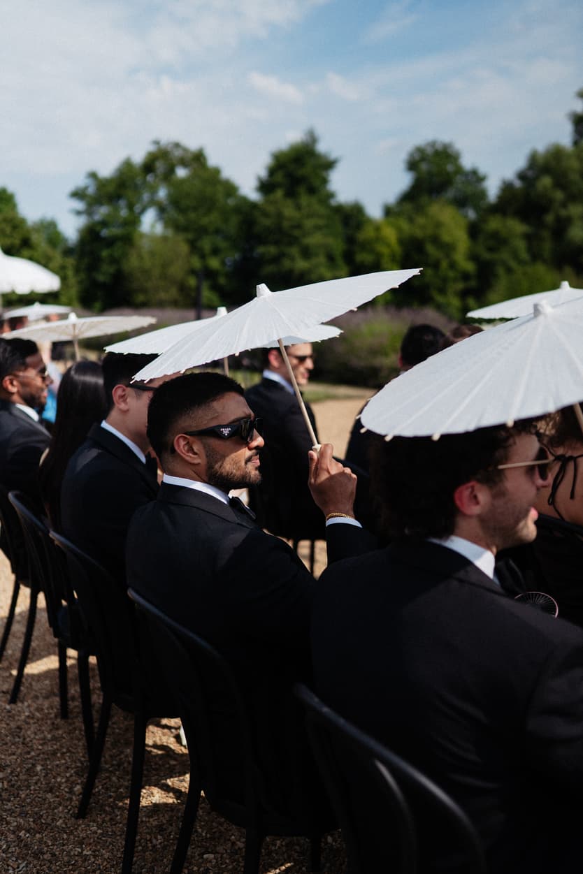 Guests in black tie under white parasols waiting for the outdoor ceremony at Château du Grand Lucé
