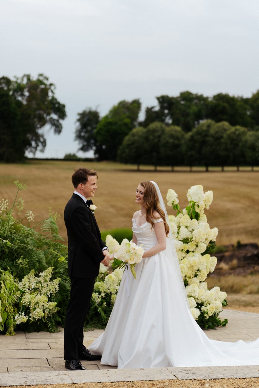 Bride and groom at the outdoor ceremony between two banks of white hydrangea, the Loire countryside behind