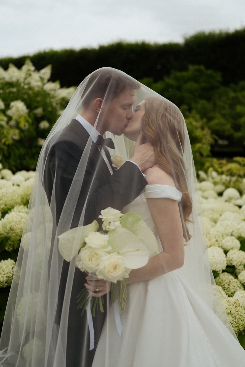 The couple kissing under her veil in front of the white hydrangea after the château ceremony