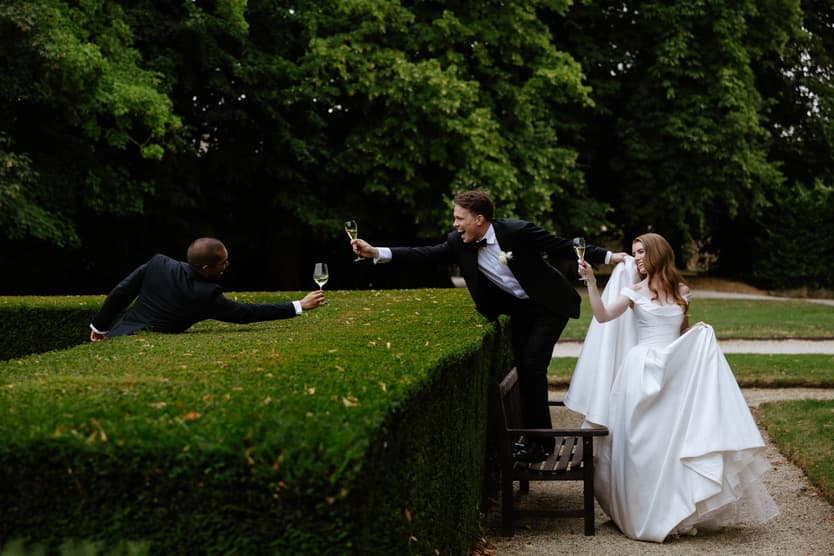 A guest lying along the topiary to pass champagne down to the groom at the cocktail hour, the bride beside him