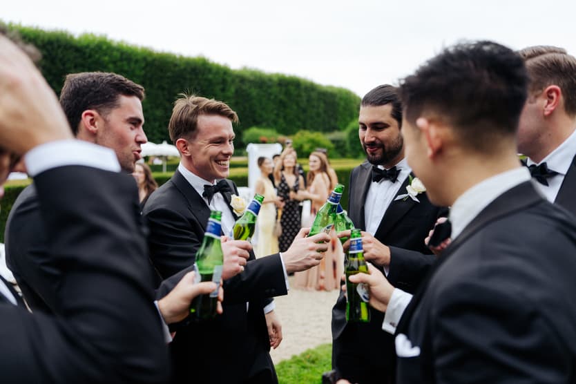 Guests in black tie with champagne against the tall topiary at a Loire Valley château wedding