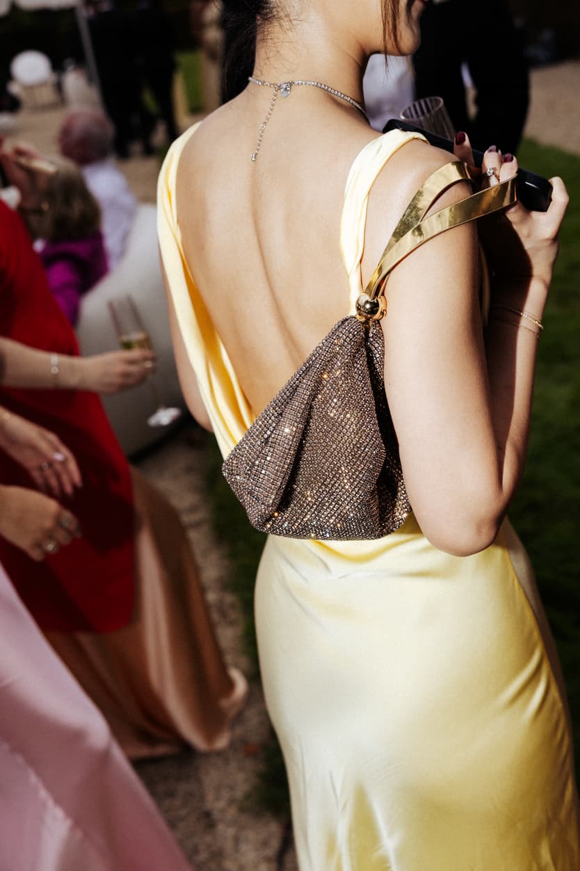 A guest at the cocktail hour in a backless yellow silk dress with a crystal necklace and gold beaded bag