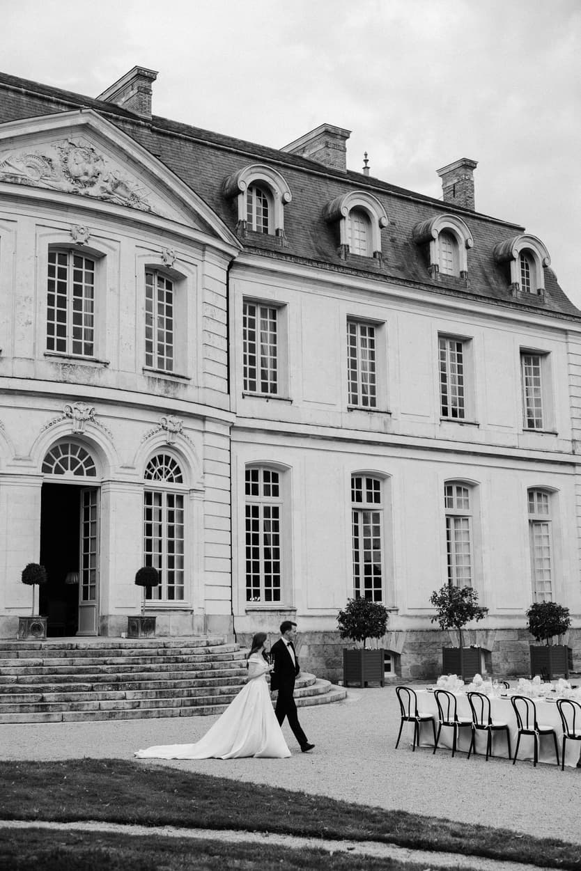 The couple crossing the gravel to the wedding dinner below the château façade, in black and white