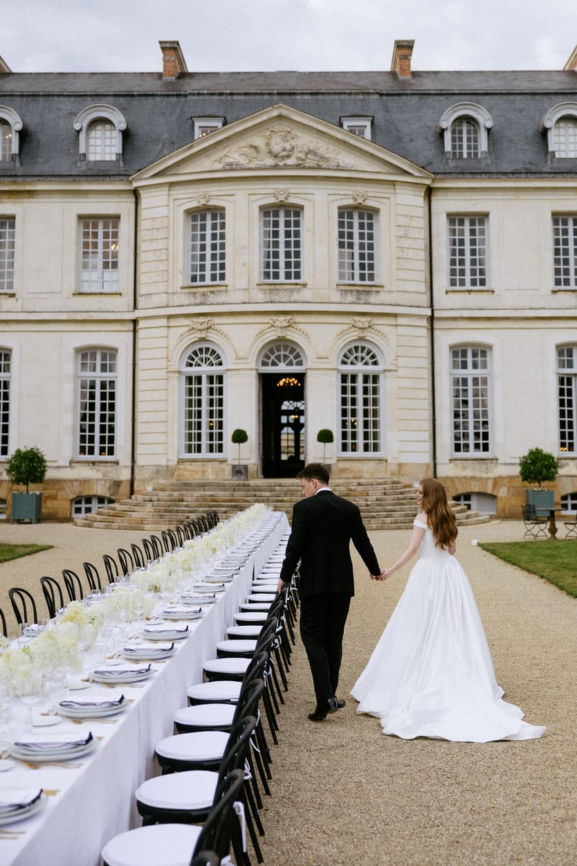 Bride and groom walking the length of the long dinner table towards the façade of Château du Grand Lucé