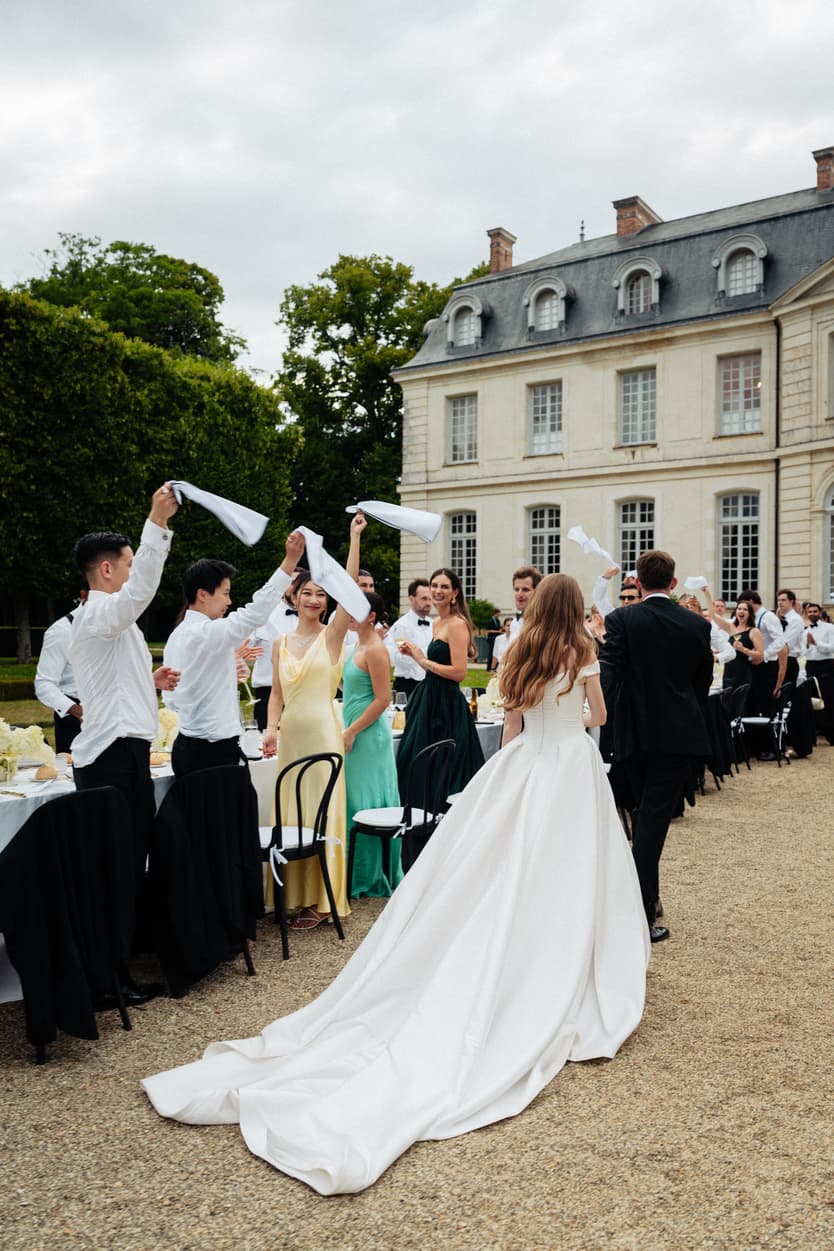A bride walking between her guests in the cour d'honneur of a château, her veil lifted behind her