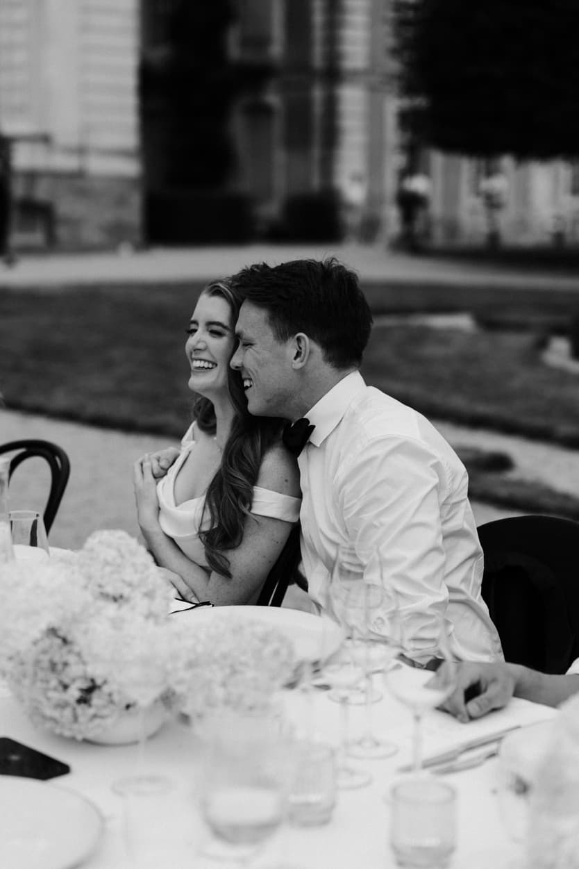 Bride and groom at the wedding dinner table in black and white, her head on his shoulder