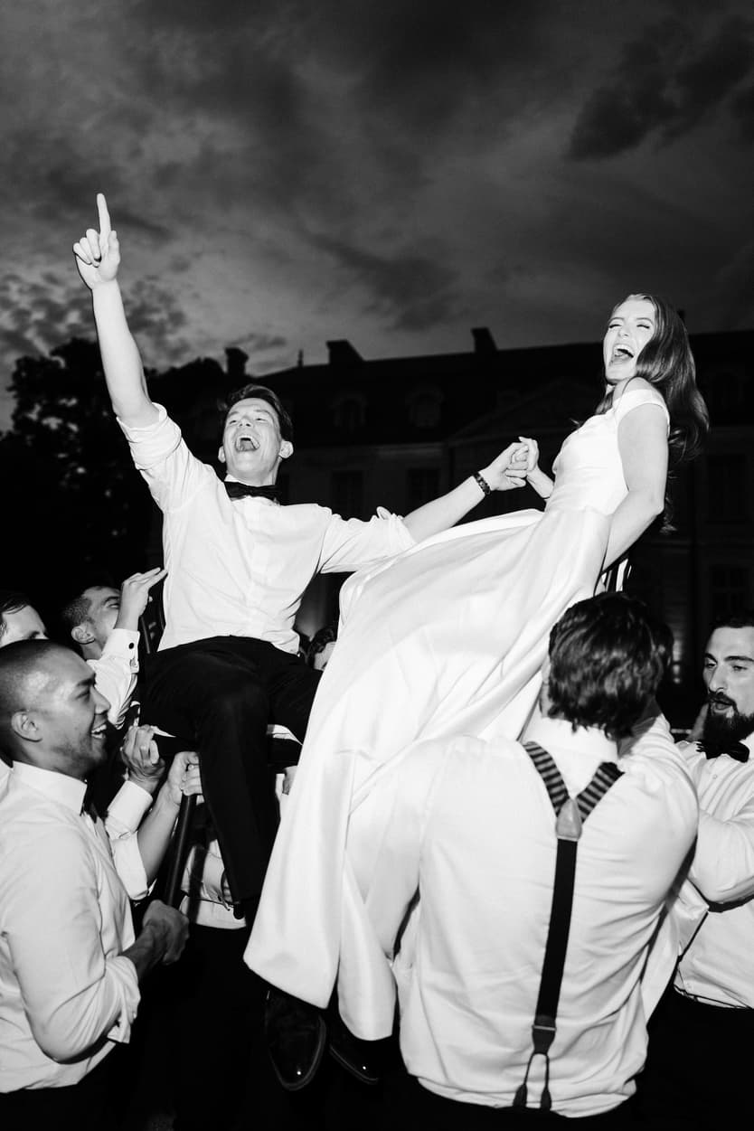 Bride and groom lifted in the air by their friends outside the château at night, in black and white