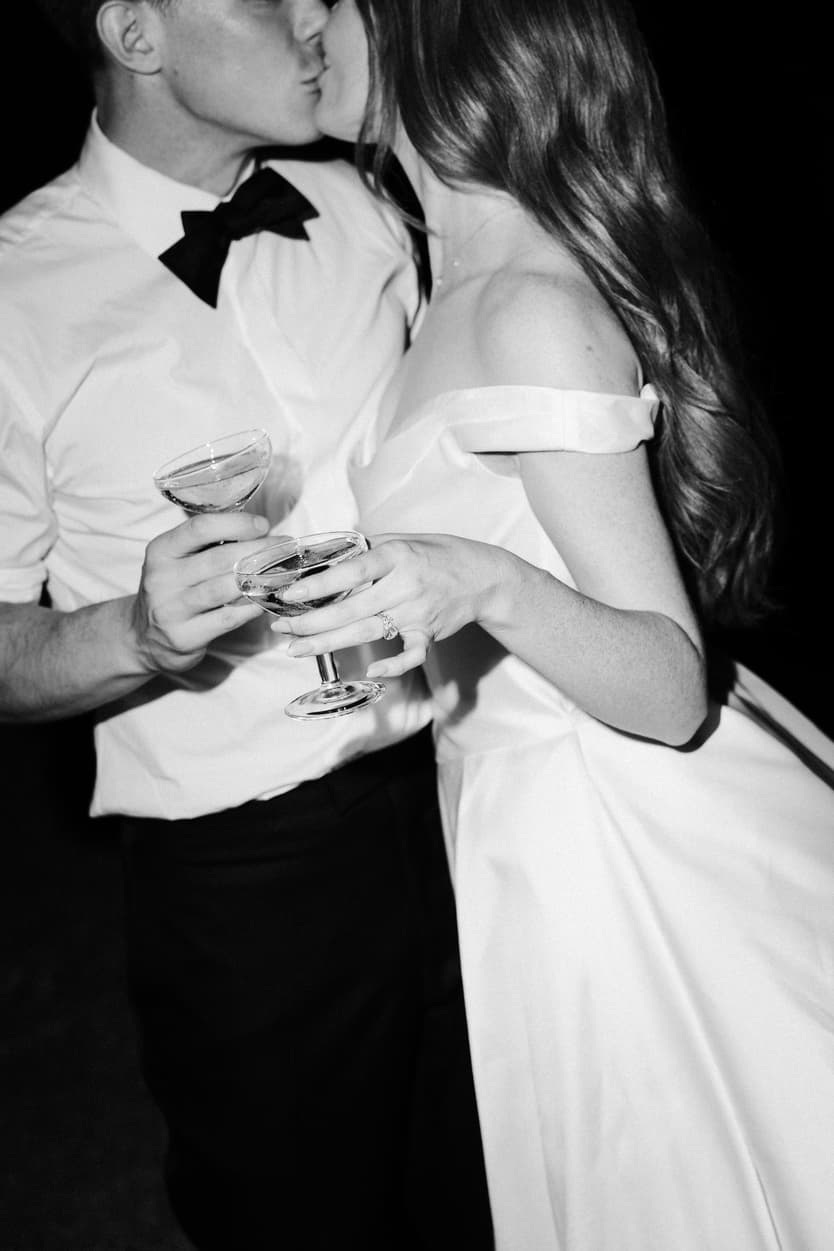 Bride and groom dancing with a glass each on the dance floor, her satin dress against his white shirt