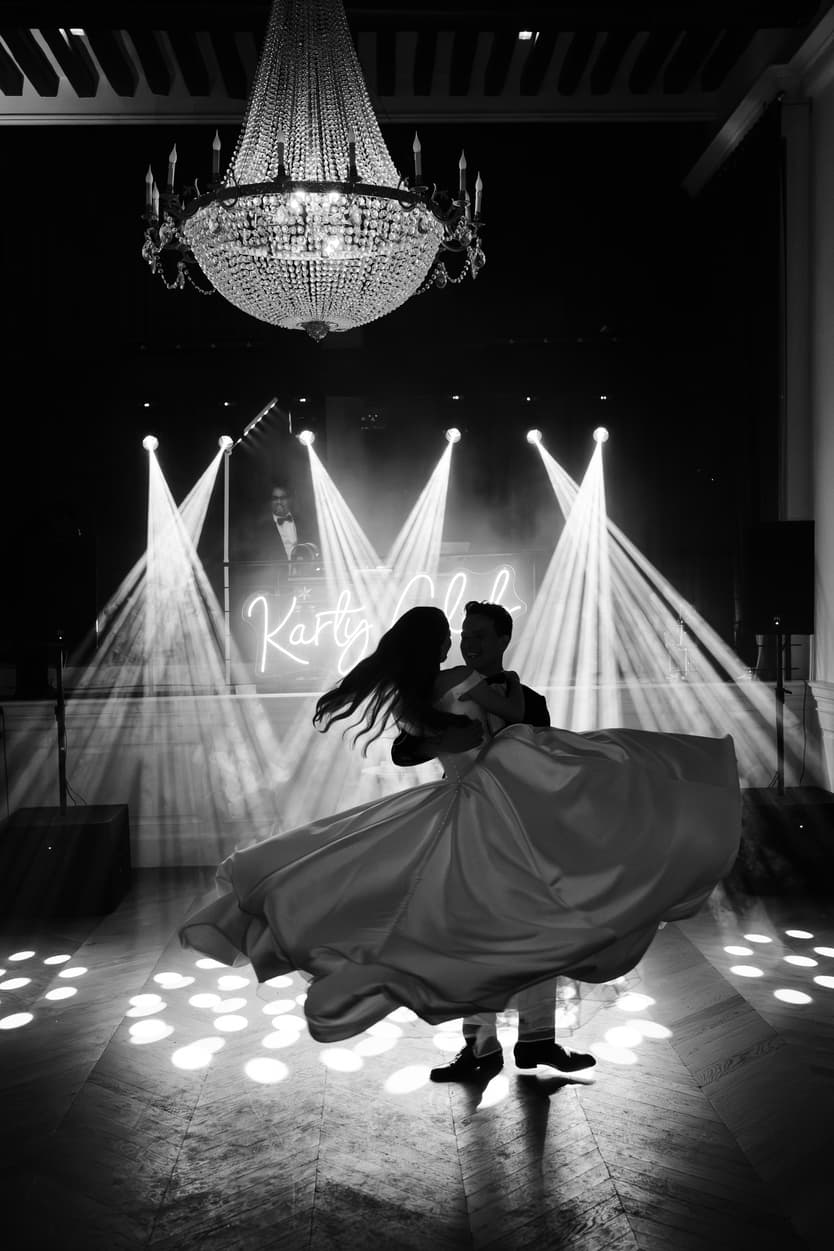 The couple dancing under the crystal chandelier, her satin skirt spinning in the spotlights below the neon sign