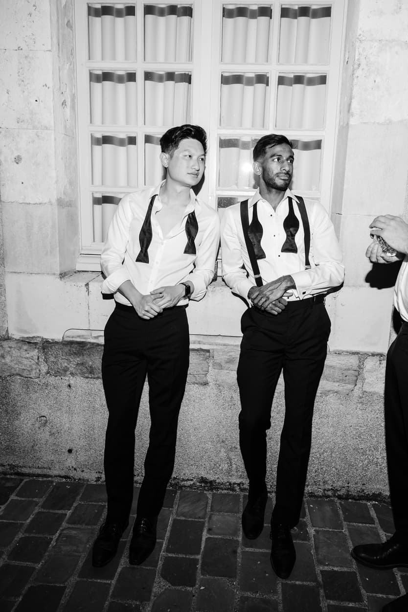 Two groomsmen with their bow ties undone against the wall of Château du Grand Lucé, in black and white