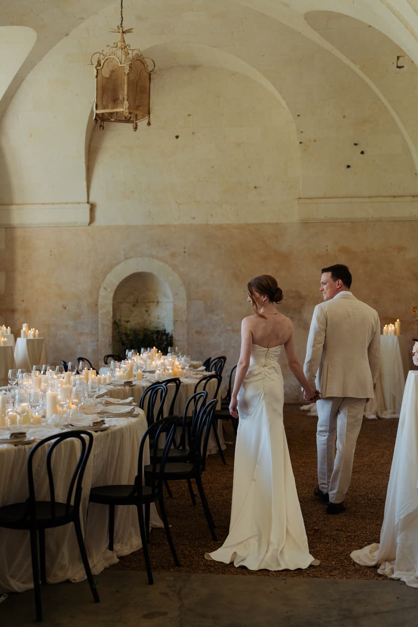 The couple walking into the candlelit orangerie for their welcome dinner, her white satin slip dress