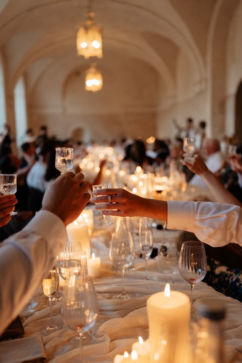 Guests raising their glasses over the candlelit welcome dinner table in the orangerie, lanterns above