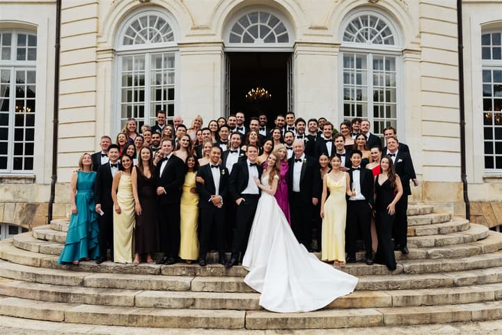 The whole wedding party on the steps of Château du Grand Lucé in black tie, the bride’s satin train down the stone